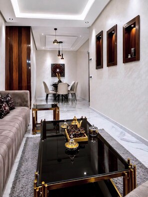 A modern living room with a sofa, a dining area with chairs, a coffee table with decorative items, and a wall with built-in shelves.
