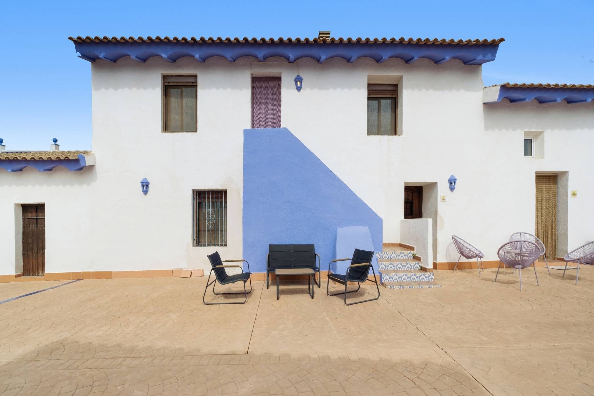 A two-story building with a blue accent wall, multiple windows, and outdoor seating with chairs and tables.