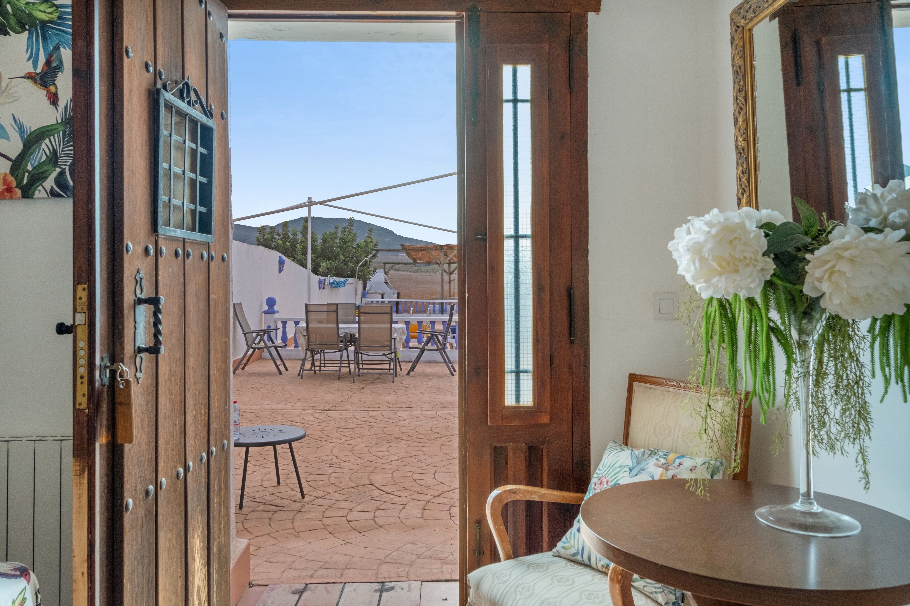 Puerta abierta que da a un patio exterior con una mesa, sillas, una parrilla y vistas a la montaña.