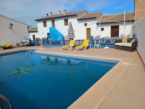Une piscine avec des chaises longues, un mur bleu et un bâtiment doté d’un toit en tuiles.