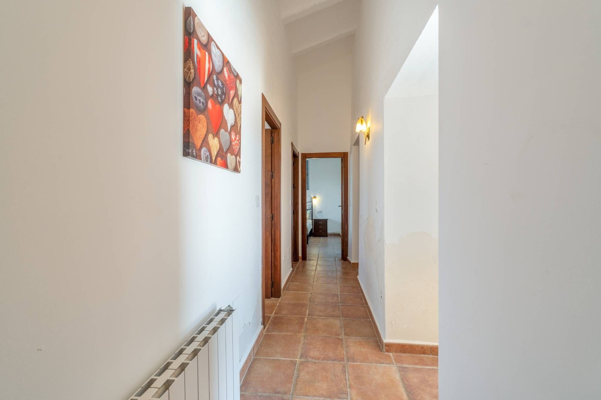 Un pasillo con suelo de baldosas, un cuadro en la pared y una puerta que da a otra habitación.