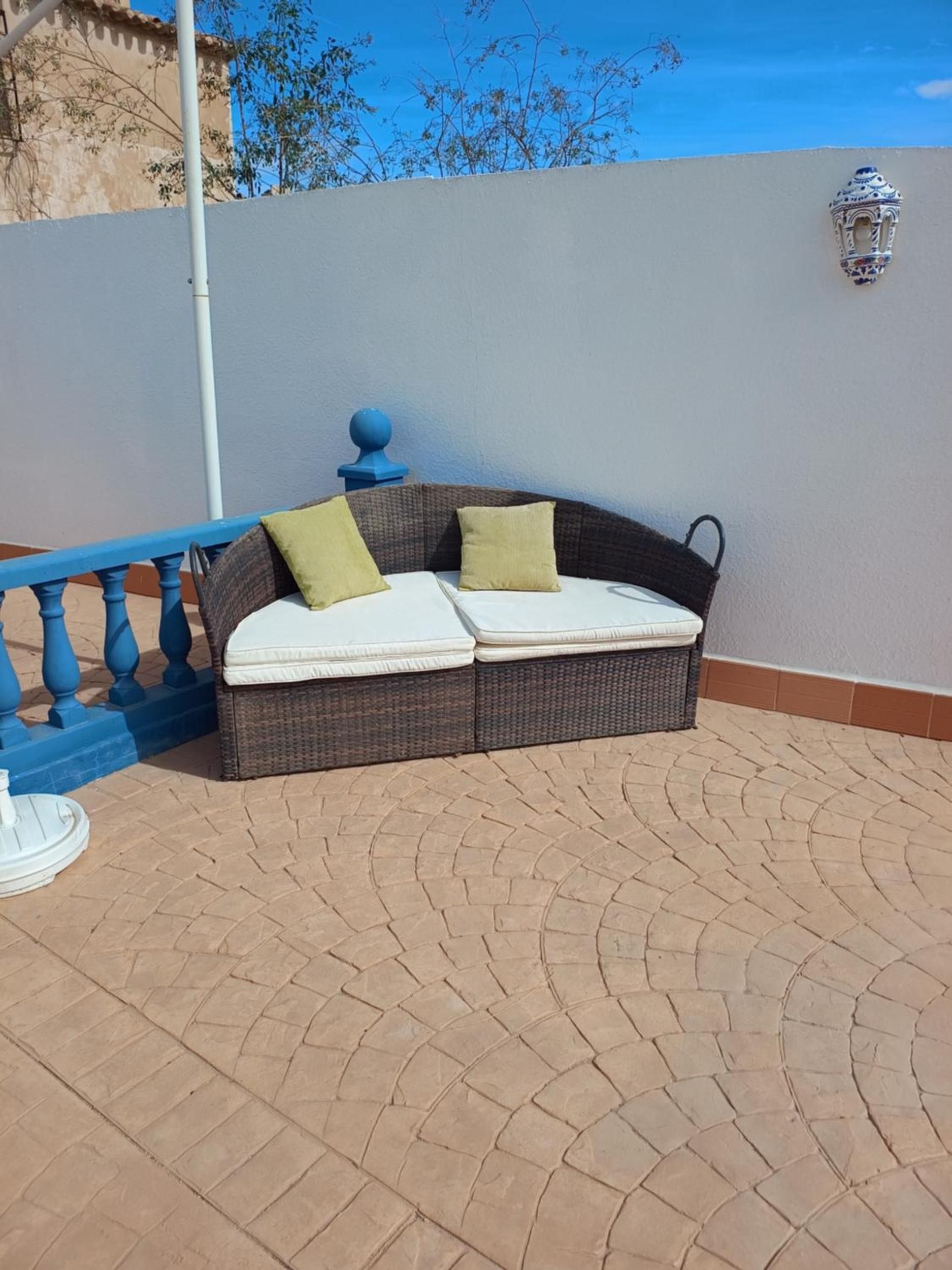 Un sofá de mimbre con cojines en un patio empedrado.