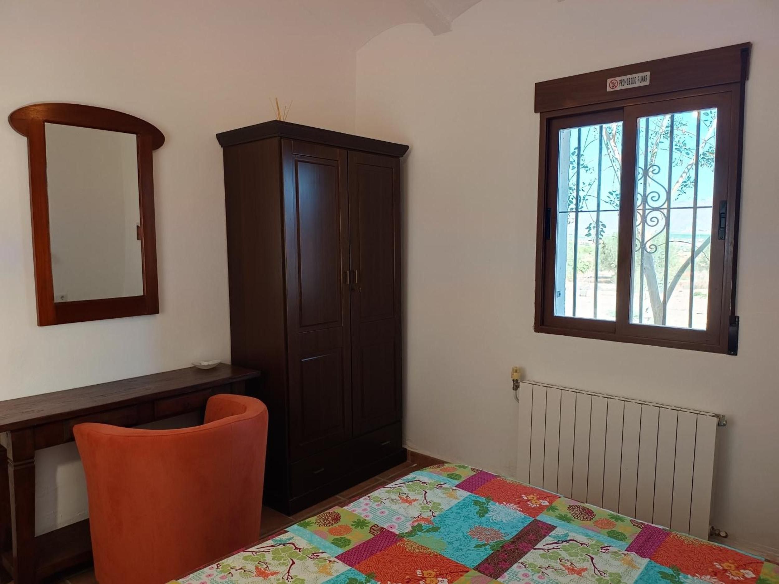 Une chambre équipée d’une armoire, d’un bureau, d’une chaise, d’un radiateur et d’une fenêtre donnant sur un paysage agréable.