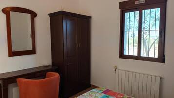 Une chambre équipée d’une armoire, d’un bureau, d’une chaise, d’un radiateur et d’une fenêtre donnant sur un paysage agréable.