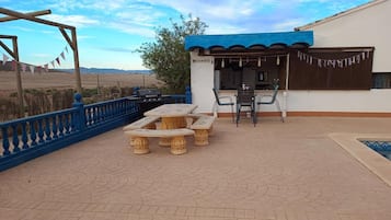 Un patio exterior con una parrilla, una mesa con sillas y una zona de piscina.