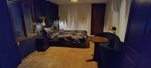 Une chambre à coucher comprenant un lit, une chaise, une petite table et une lampe décorative.