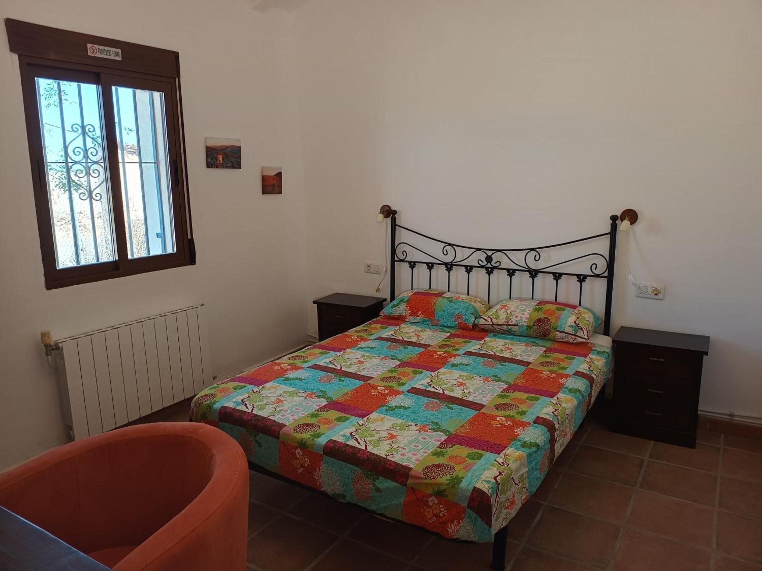 Un dormitorio con cama, mesita de noche, silla, ventana y radiador.