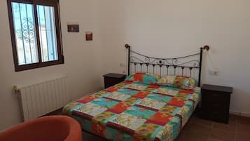 Un dormitorio con cama, mesita de noche, silla, ventana y radiador.