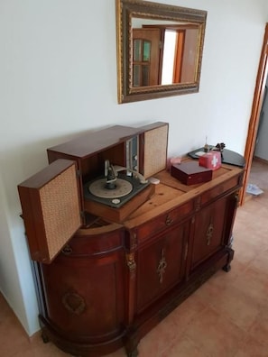 A wooden cabinet with a mirror above it, a radio on top, and a red object on the right. - YARD (Amora)