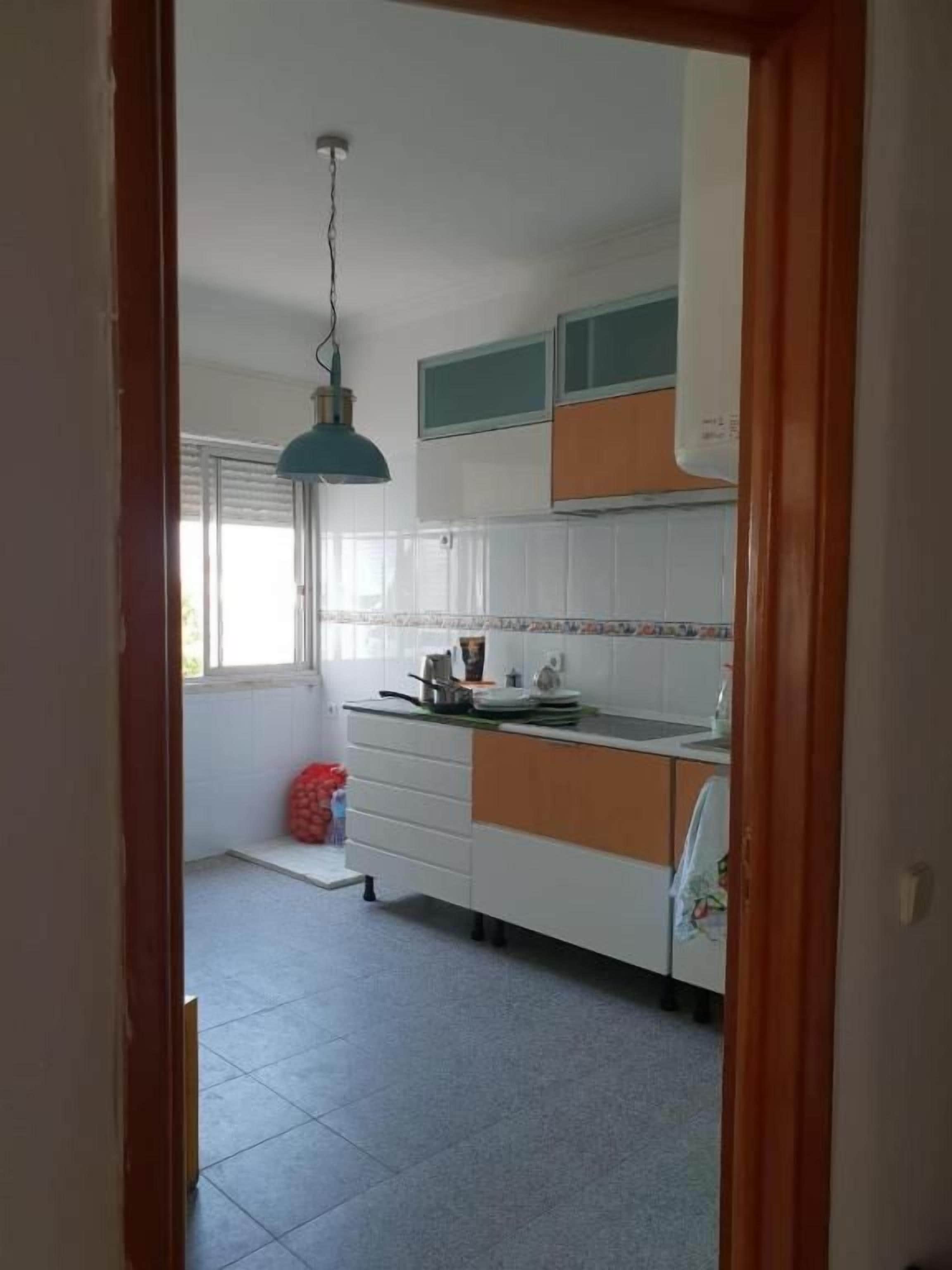 A kitchen with white cabinets, a hanging light fixture, and a window with blinds.