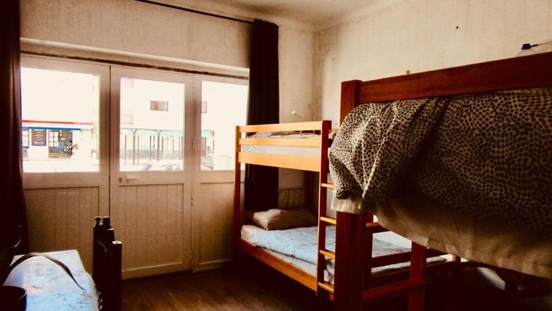 Una habitación con literas, piso de madera y ventana con vista a un edificio.