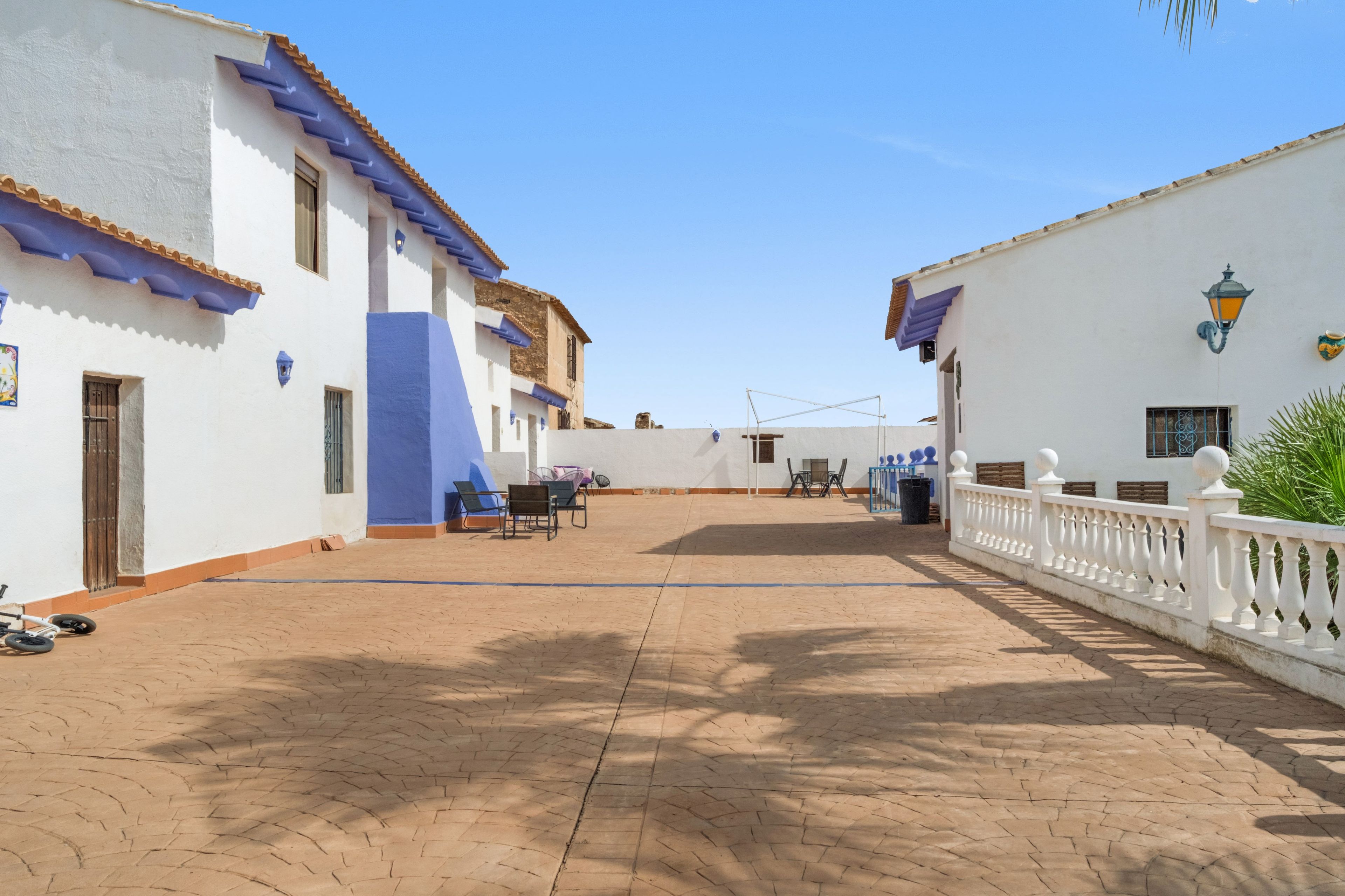 Un patio con un sendero adoquinado, edificios blancos con detalles azules y una valla blanca.
