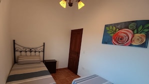 Une chambre avec deux lits, une porte en bois, une table de chevet et un tableau accroché au mur.