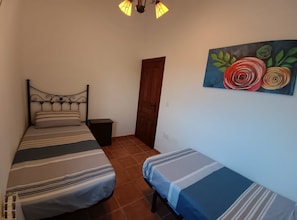 Een slaapkamer met twee bedden, een houten deur, een nachtkastje en een schilderij aan de muur.