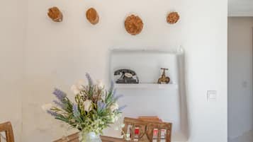 A dining area with a table, chairs, a vase with flowers, and a wall-mounted shelf with a telephone and a decorative item.