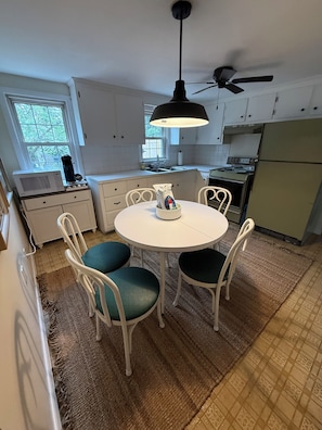 A kitchen with white cabinets, a white dining table with four chairs, a ceiling fan, and a window with a view of trees. - NEW in 2026: Cozy Oasis- great backyard, near Dennis Beaches, Great Restaurants (Dennis)