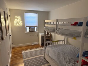 A bedroom with bunk beds, a window with blinds, a desk, and a wall-mounted air conditioner. - NEW in 2026: Cozy Oasis- great backyard, near Dennis Beaches, Great Restaurants (Dennis)