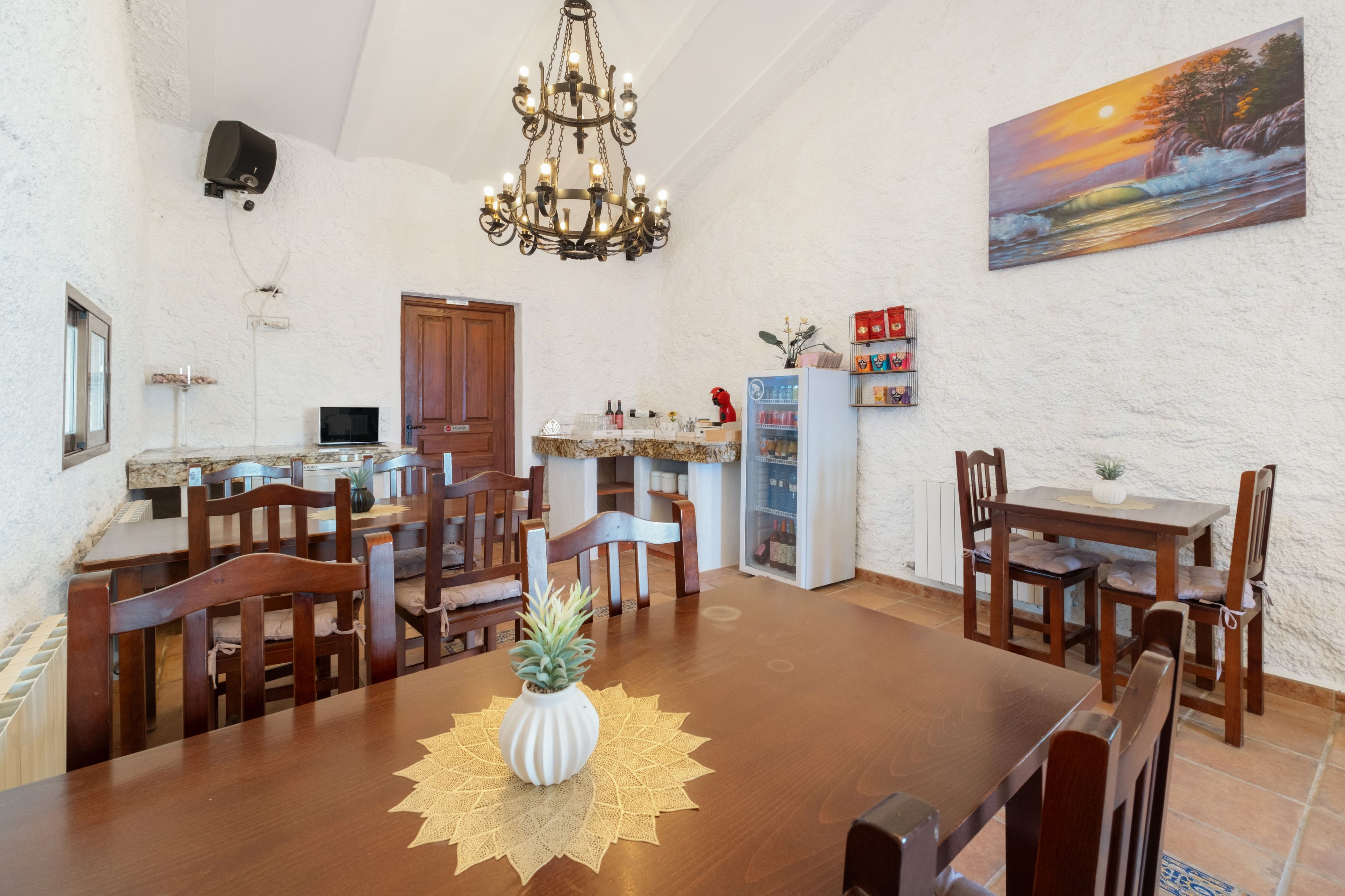 A dining area with a wooden table, chairs, a chandelier, a painting, and a refrigerator.