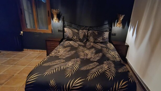 A bed with a leaf pattern bedspread, a dark headboard, and a window with blinds. - Room 'Calabaza' with Mountain View, Wi-Fi and Air Conditioning (Lorca)