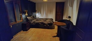 Een compacte slaapkamer met een bed, een klein rond tafeltje en een stoel.