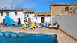 A swimming pool with lounge chairs and umbrellas, surrounded by buildings with tiled roofs. - Room 'Calabaza' with Mountain View, Wi-Fi and Air Conditioning (Lorca)