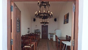 Zona pranzo con tavoli e sedie in legno, un lampadario e pavimento piastrellato.