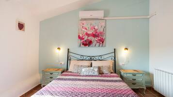 A bedroom with a bed, two bedside tables, a wall-mounted air conditioner, and a painting.