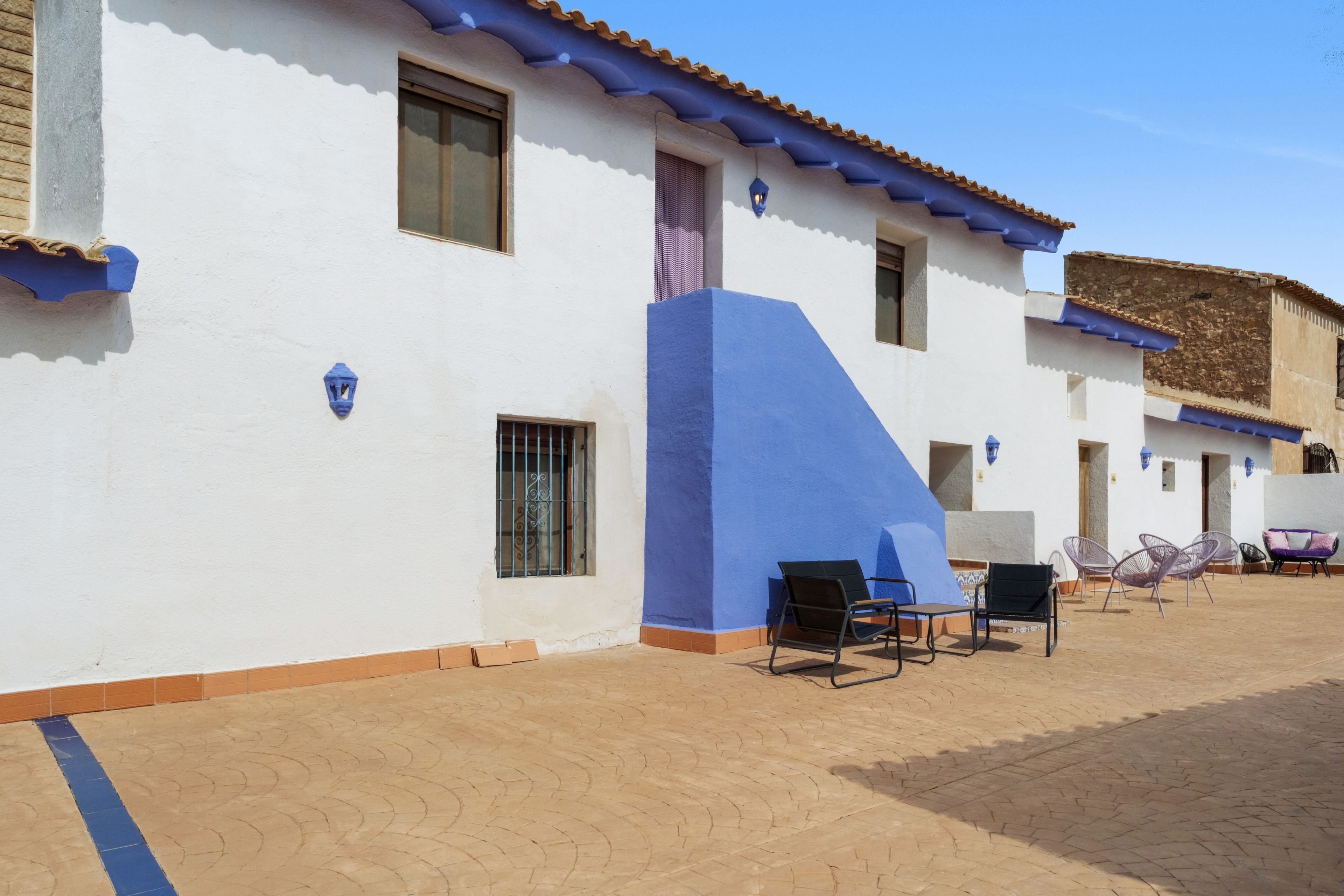 A building with a white exterior and blue accents, featuring a patio area with outdoor seating.