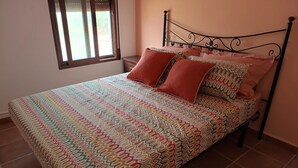 Un letto con copriletto decorato e due cuscini, un comodino e una finestra con persiane.