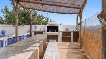 An outdoor kitchen area with a grill, a tiled bench, and a pergola structure.
