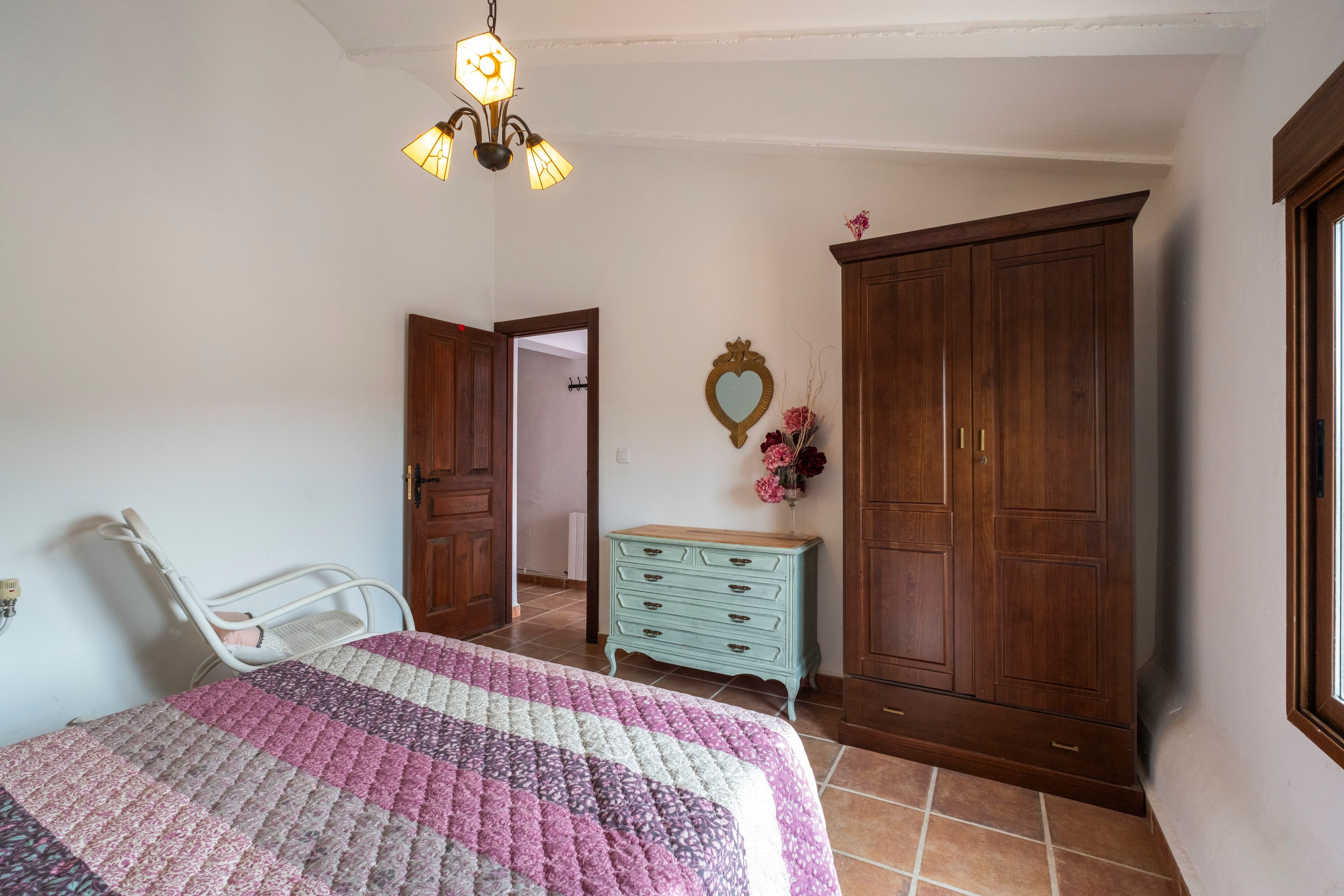 Una camera da letto con un letto, una cassettiera, un armadio e una lampada a sospensione.