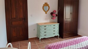 Una camera da letto con un'armadio in legno, una cassettiera chiara, uno specchio a forma di cuore e una coperta a letto rosa e bianca.