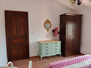 Une chambre à coucher avec une armoire en bois, une commode de couleur claire, un miroir en forme de cœur et une couverture rose et blanche sur le lit.