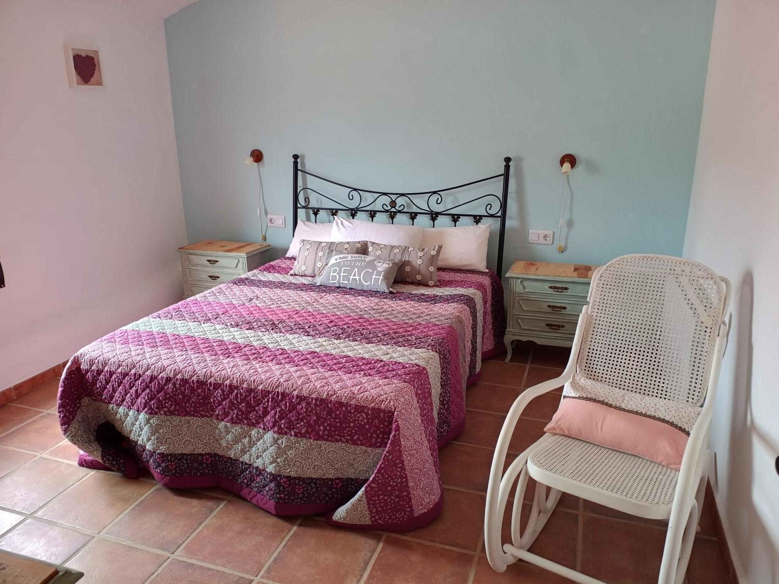 Une chambre à coucher comprenant un lit, deux tables de chevet, une chaise et un luminaire fixé au mur.