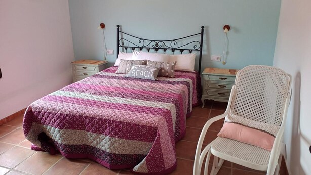 Una camera da letto con un letto, due comodini, una sedia e un punto luce a parete.