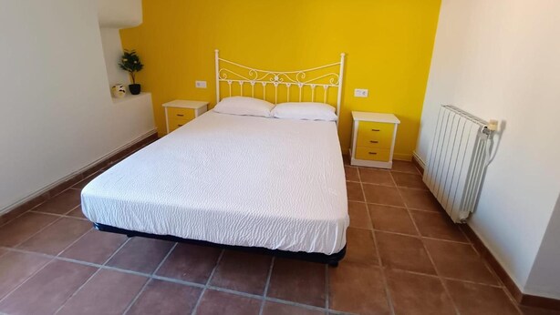 Une chambre à coucher comprenant un lit, deux tables de chevet, un radiateur et un climatiseur fixé au mur.