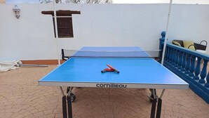 Une table de ping-pong avec un filet, posée sur une surface pavée, avec une rambarde bleue et un mur en arrière-plan.