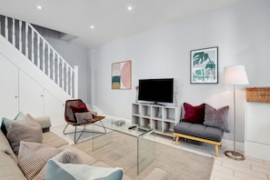 Un salon moderne avec un escalier, un téléviseur à écran plat et un canapé agrémenté de coussins.