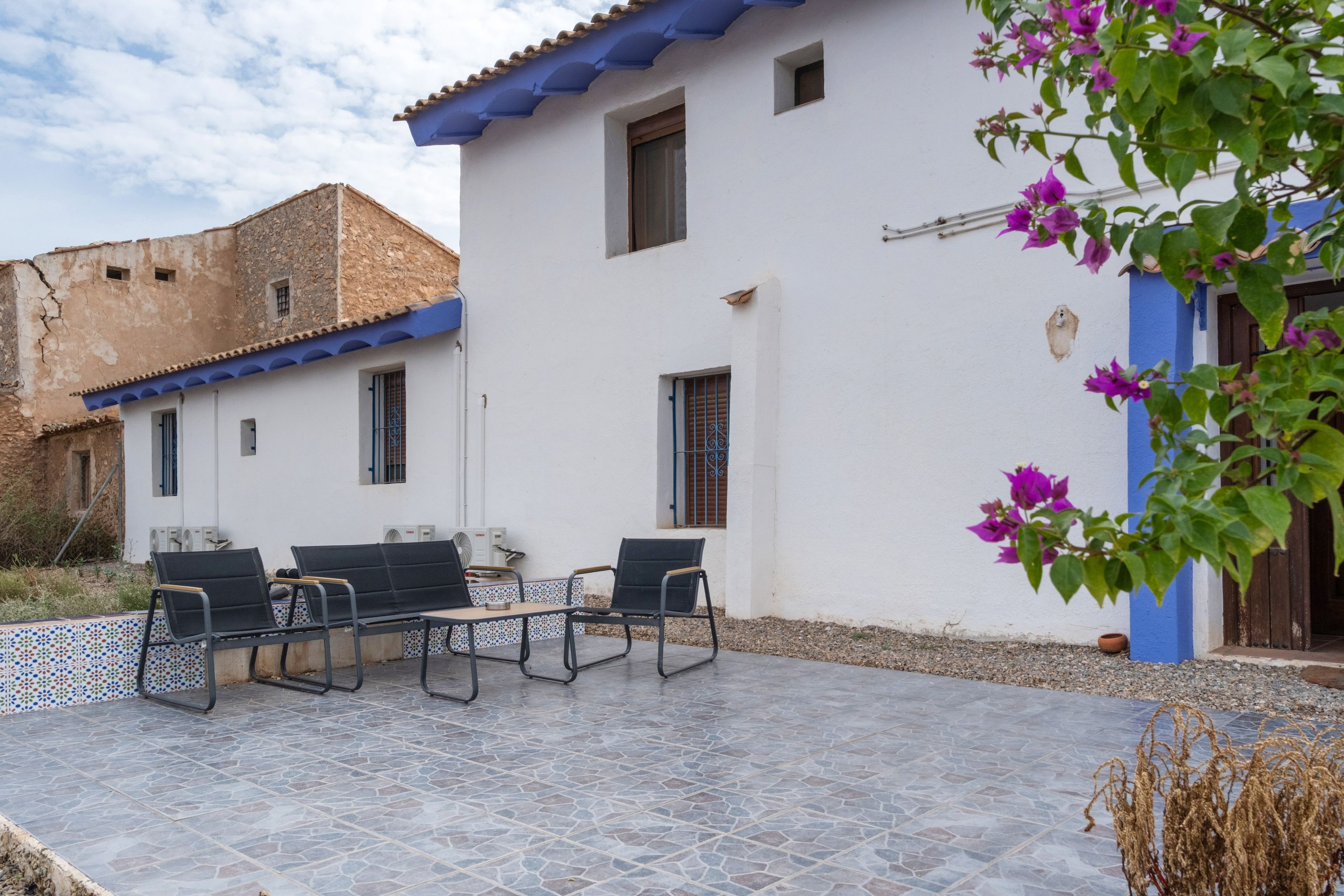 Un patio con mobiliario exterior y un edificio blanco con detalles azules.