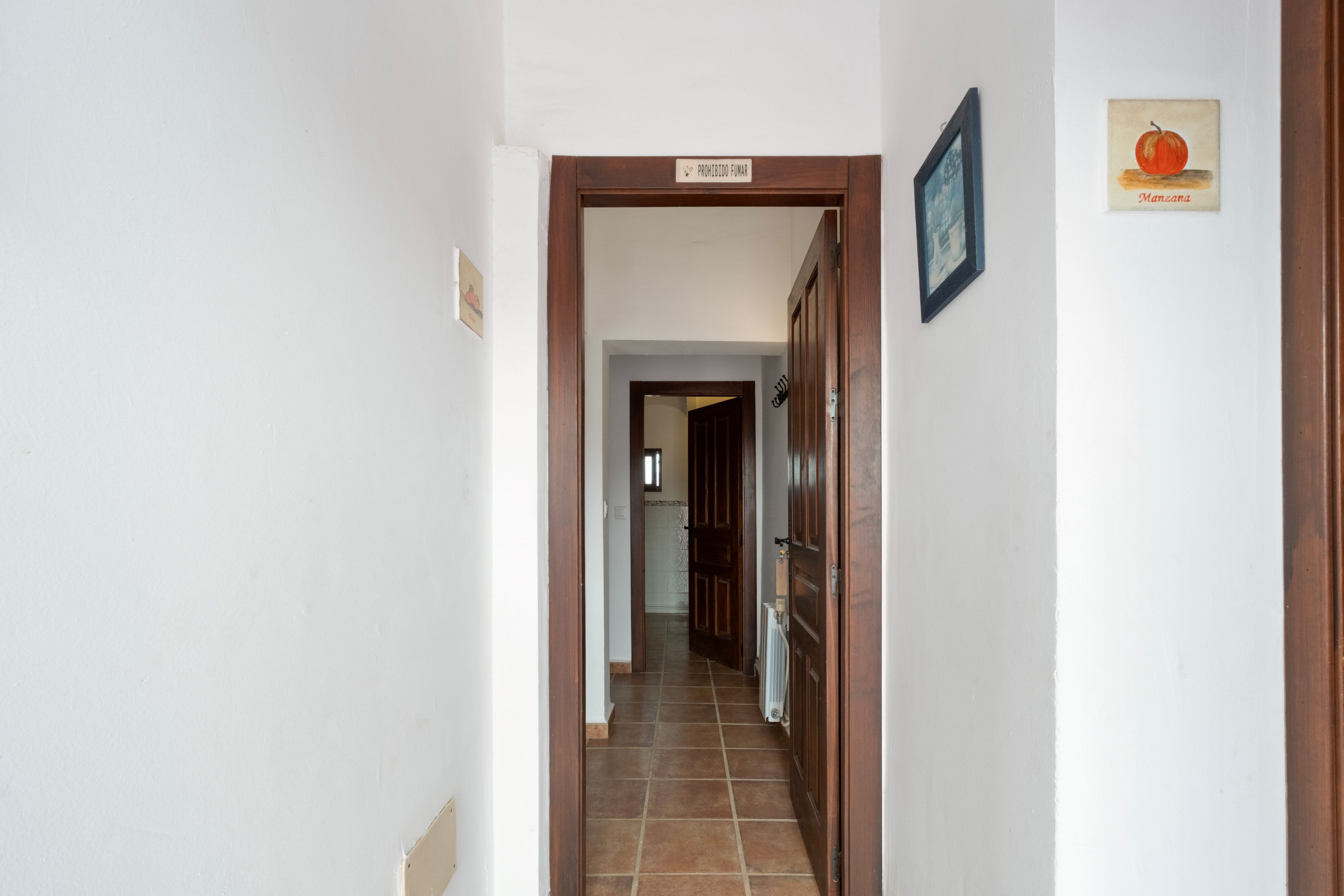 Un pasillo con una puerta de madera que indica 'PROHIBIDO FUMAR' y un cuadro con una calabaza en la pared.