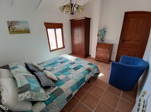 Een slaapkamer met een bed, een stoel, een garderobe, een dressoir en een raam.