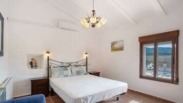A bedroom with a bed, bedside tables, a radiator, a window with a view, and a chandelier.
