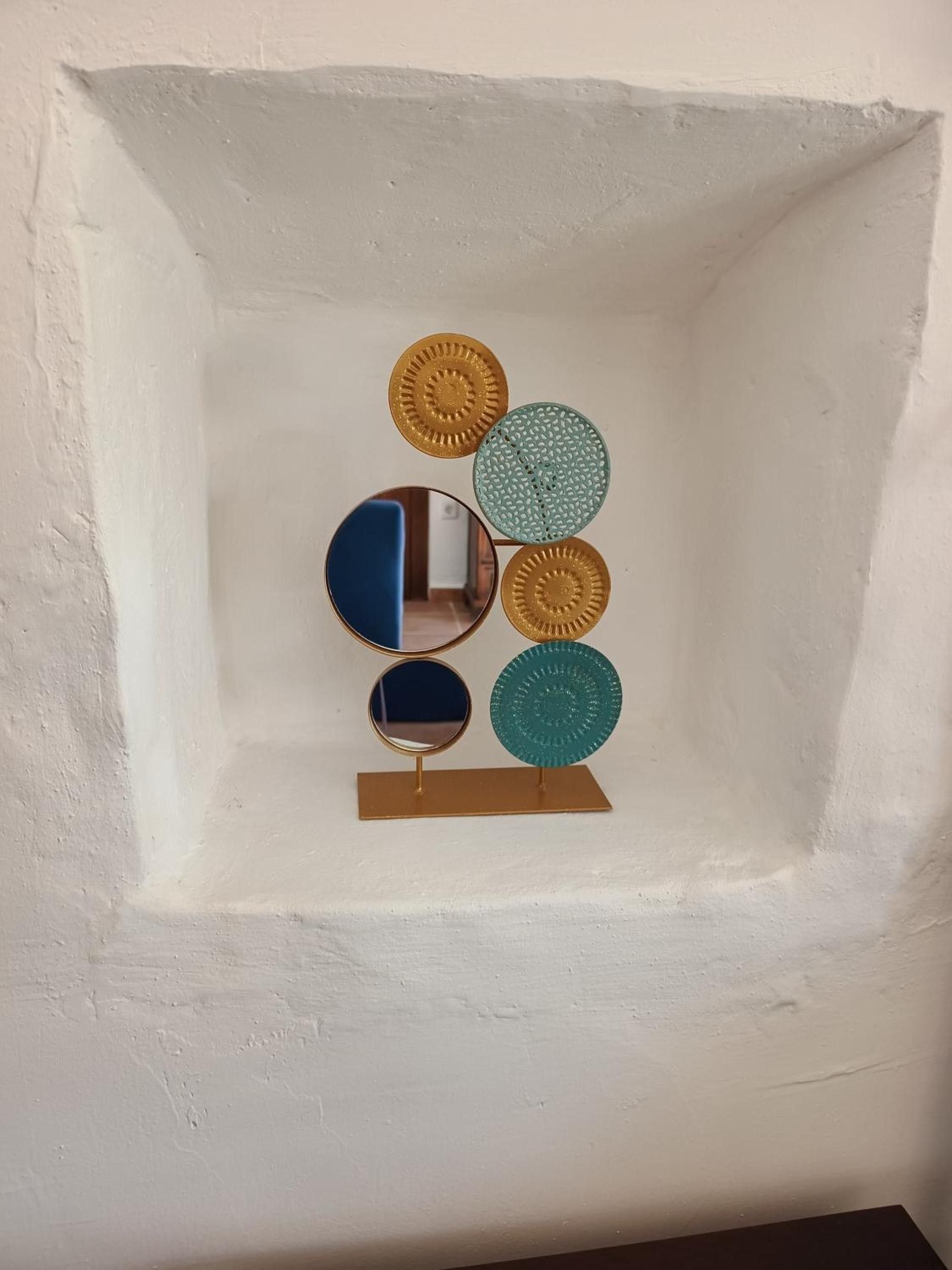 Pared con marco blanco y una instalación artística geométrica con espejos circulares y discos metálicos.
