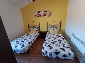 Een kamer met twee eenpersoonsbedden, elk met een bedovertrek met een geometrisch patroon, een kunstwerk aan de muur boven de bedden en een radiator.