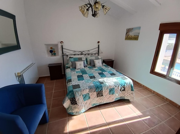 Een slaapkamer met een bed, een stoel, een radiator, een raam en een plafondlamp.