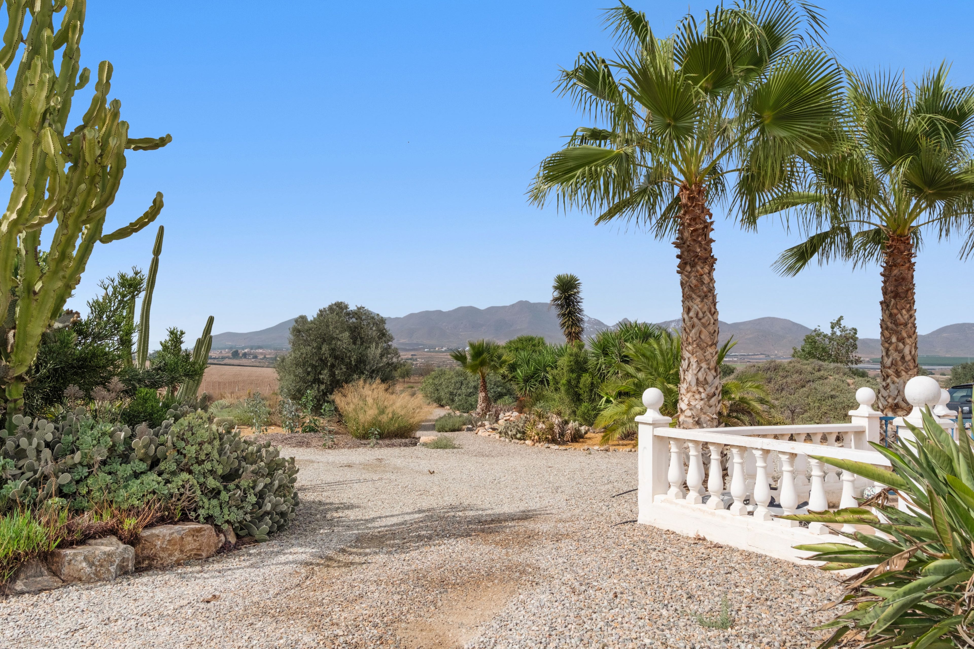 A gravel pathway leading to a white fence with a view of mountains in the distance.