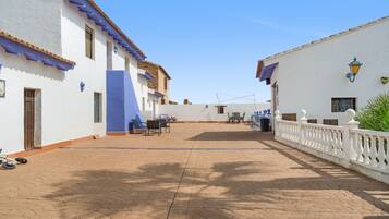 A courtyard with a paved walkway, white buildings with blue accents, and a white fence.