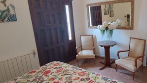 Una habitació amb un llit, dues cadires, una taula petita, un mirall i una porta.