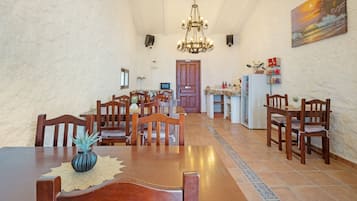 Een eetruimte met een houten tafel, stoelen, een kroonluchter en een keuken op de achtergrond.