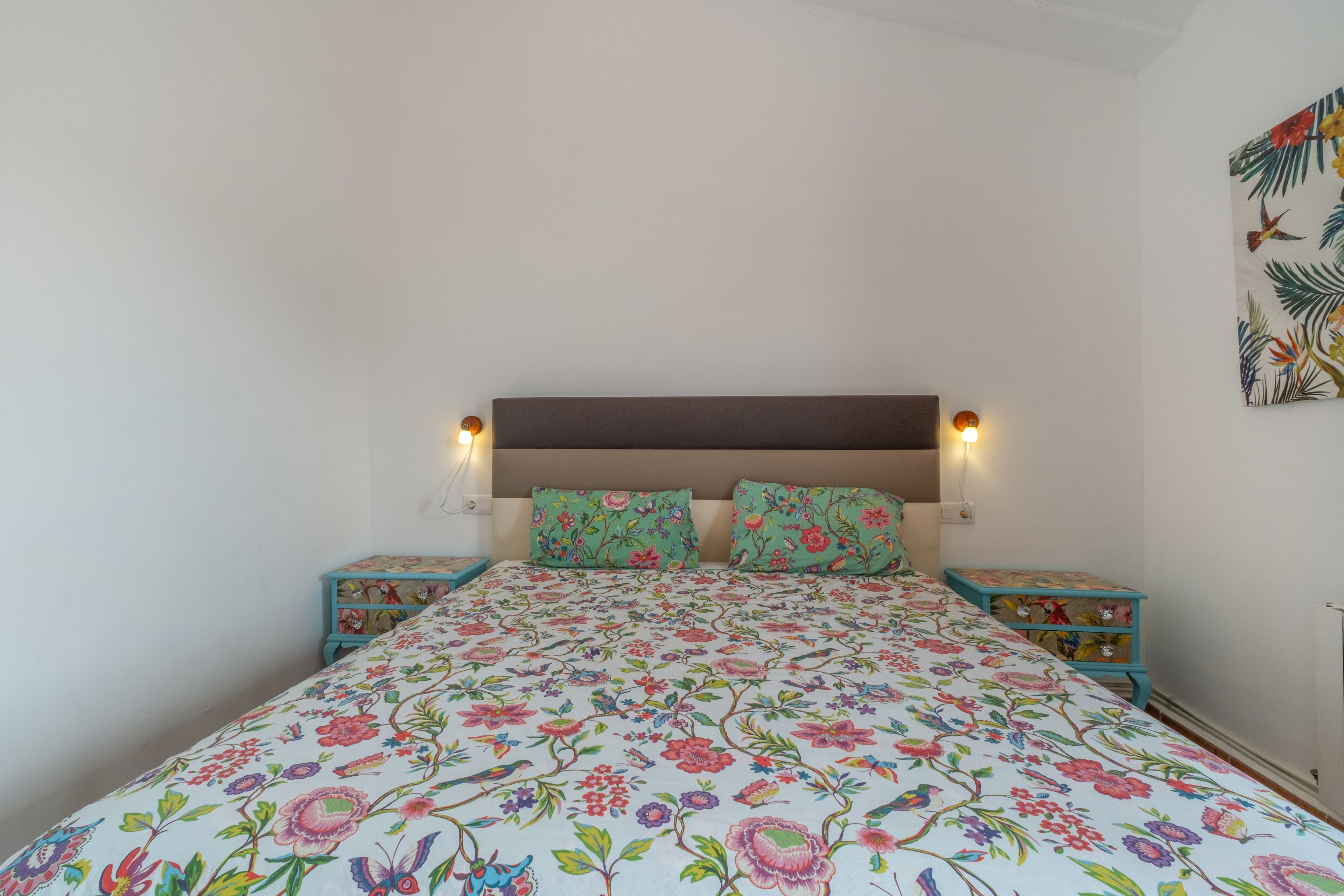 Ein Bett mit blumigem Bettzeug, zwei Nachttische mit Lampen und ein Wandbild.